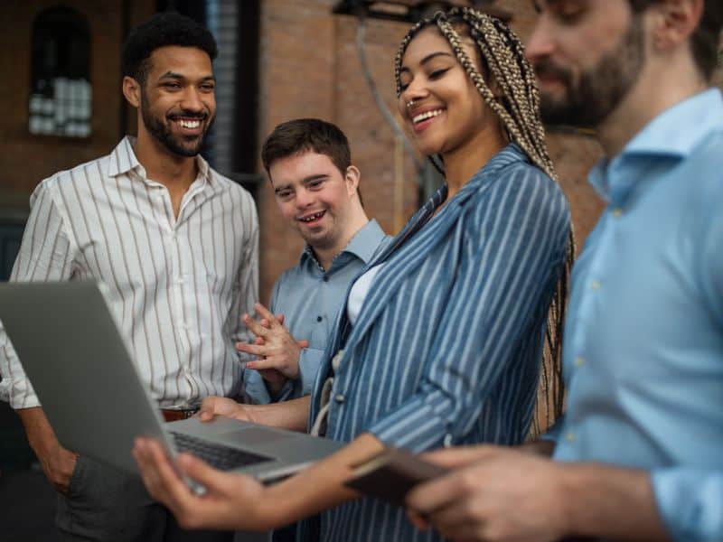 Four people looking at a laptop screen and smiling