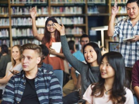 A group of students with their hands in the air ready to ask questions