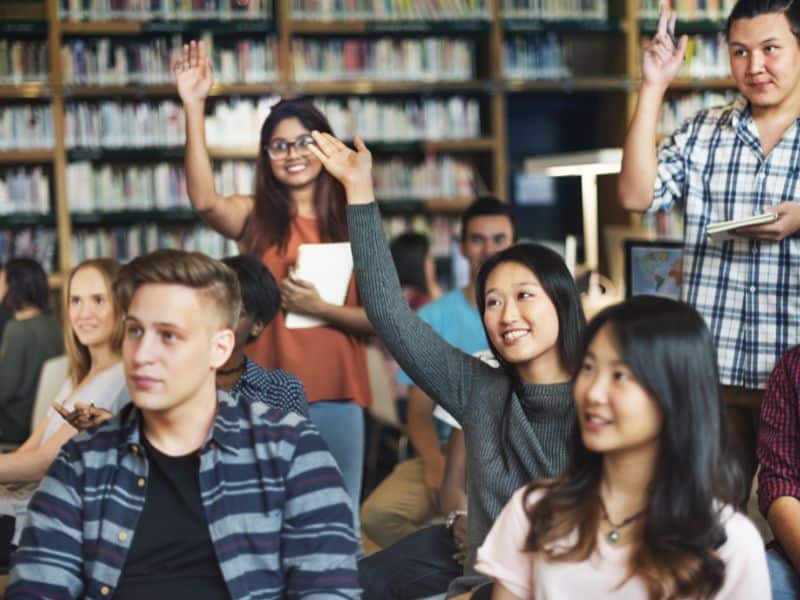 A group of students with their hands in the air ready to ask questions