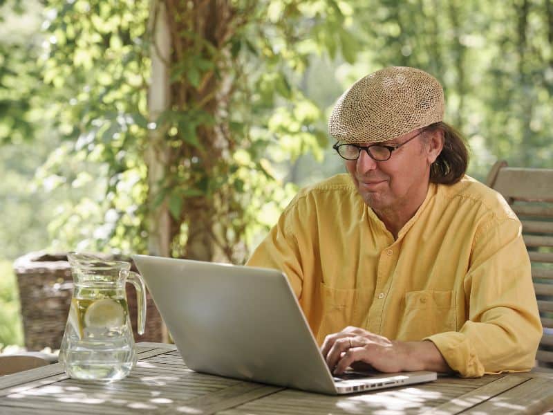 Man, wearing a cap, sitting outside reading a laptop