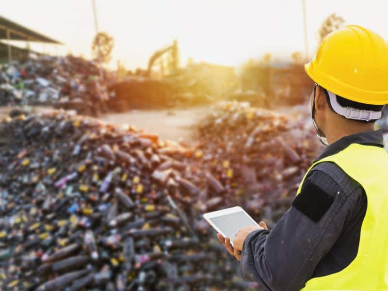 Man standing with tablet looking at a waste site.