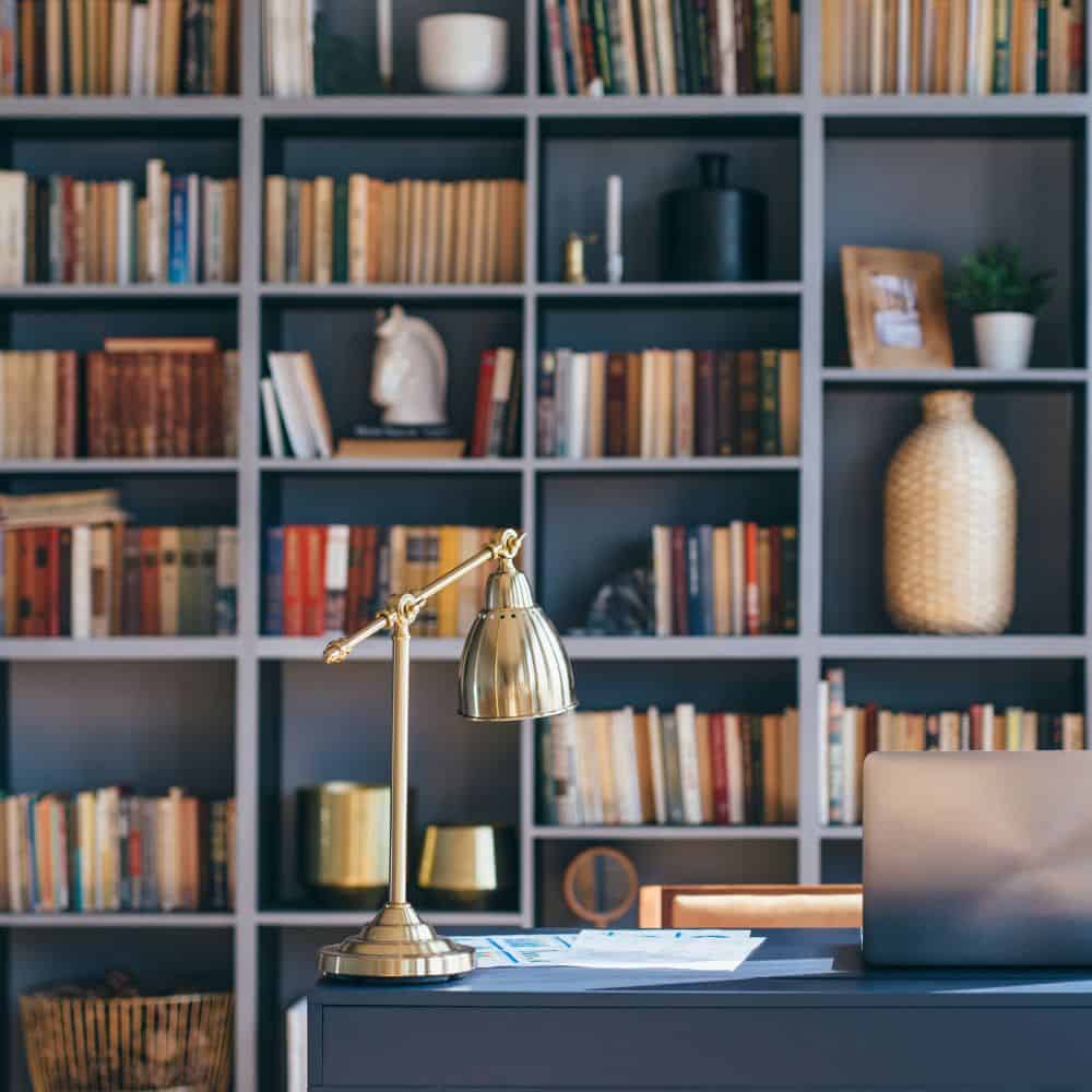 Office with bookshelves behind a desk with lamp and laptop.