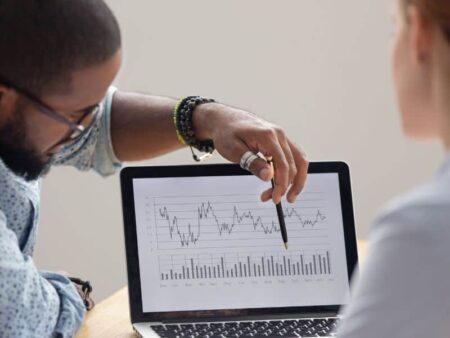 Man pointing at laptop screen showing graphs and charts.