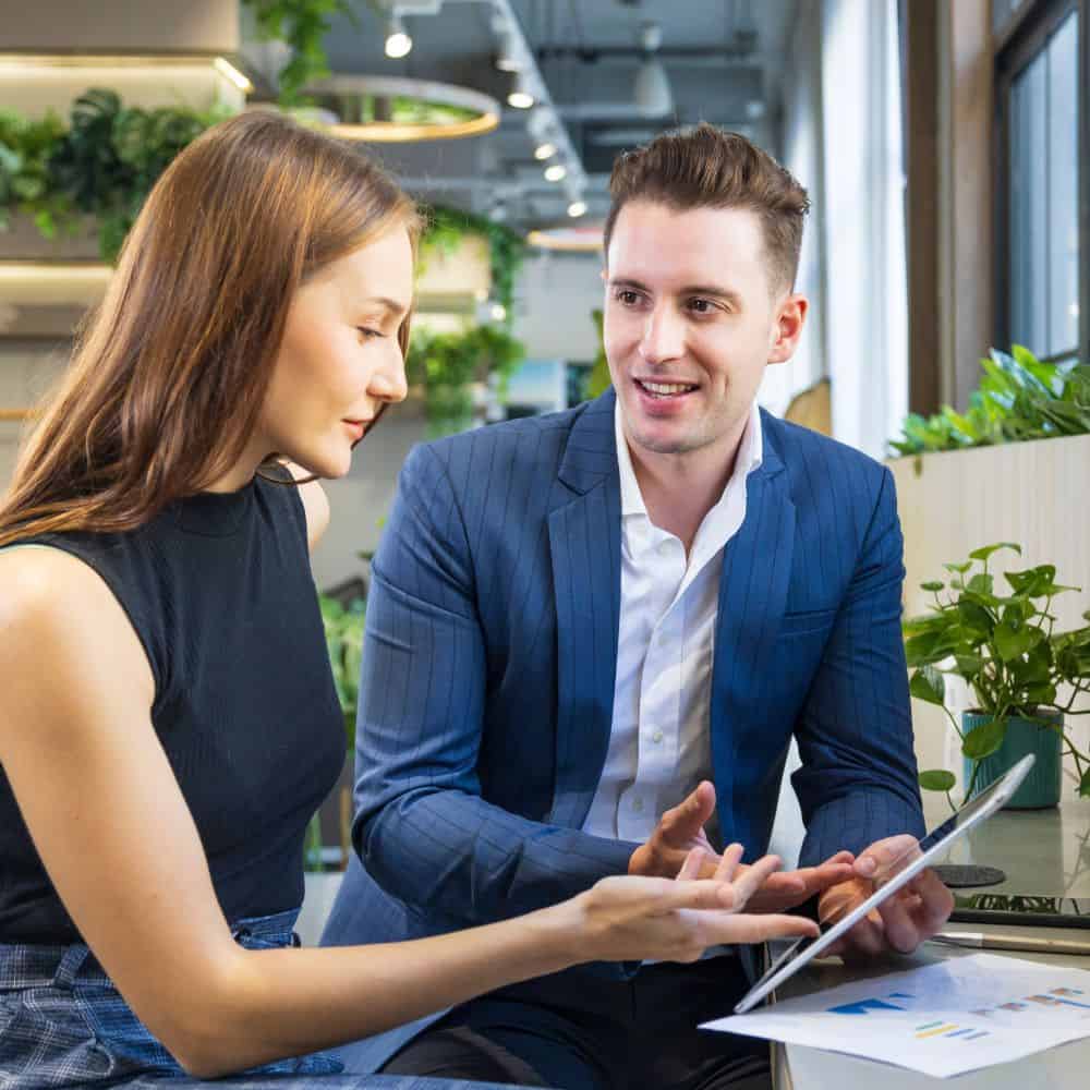 Two people in an office talking and looking at a tablet device