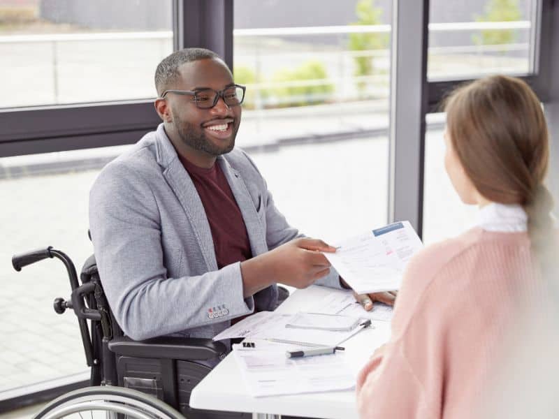 Image of a man in a wheelchair at a table talking to a woman