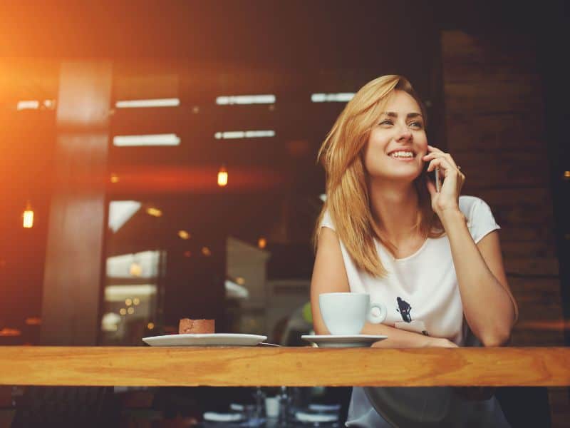 Young woman in a cafe speaking on her phone and smiling