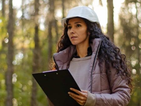 Woman forester wearing a hard hat and holding a clipboard