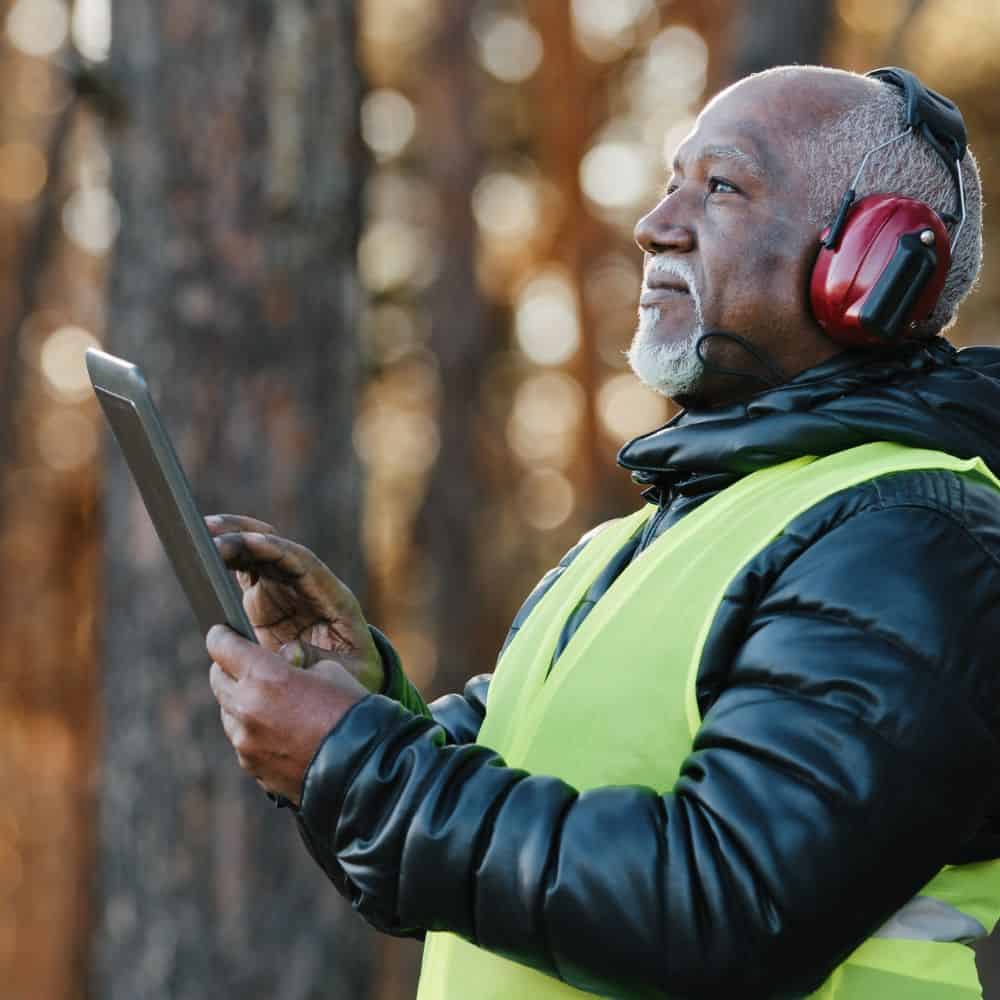 Forester with headphones and hi-vis looking at a tablet