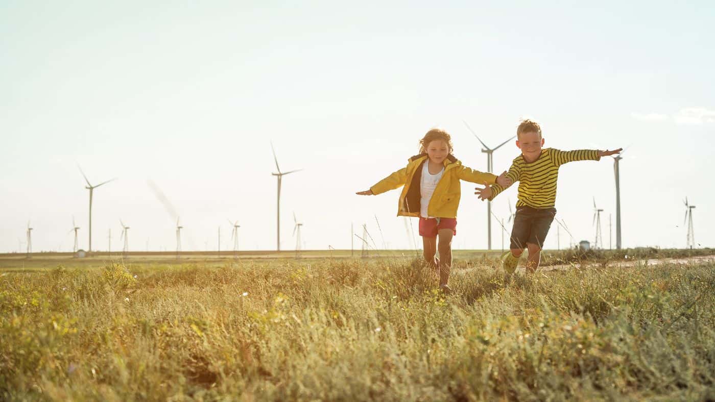 Girl and boy run in a field in from of wind turbines