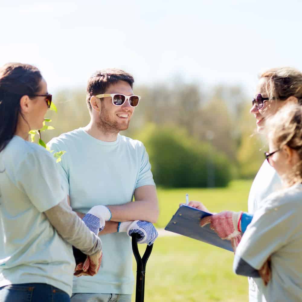 Smiling volunteers outside with clipboard and spade