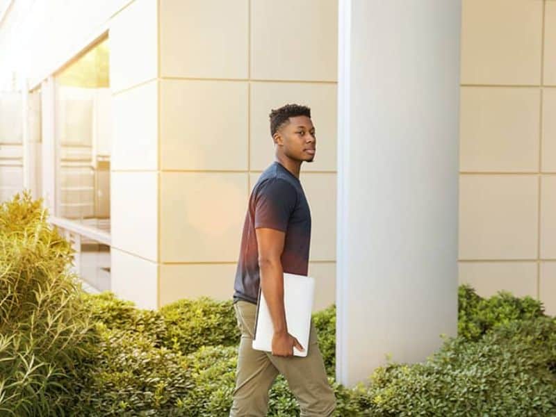 Image of man walking into a building holding a laptop