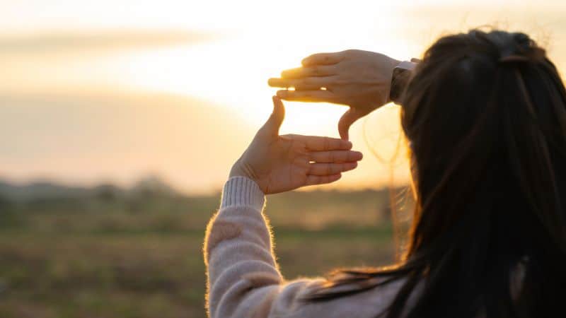 Woman creating a frame with her hands and looking into the distance outdoors