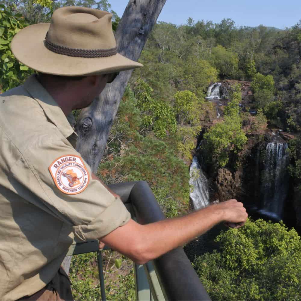 Ranger wearing uniform is leaning on a fence and looking out over park