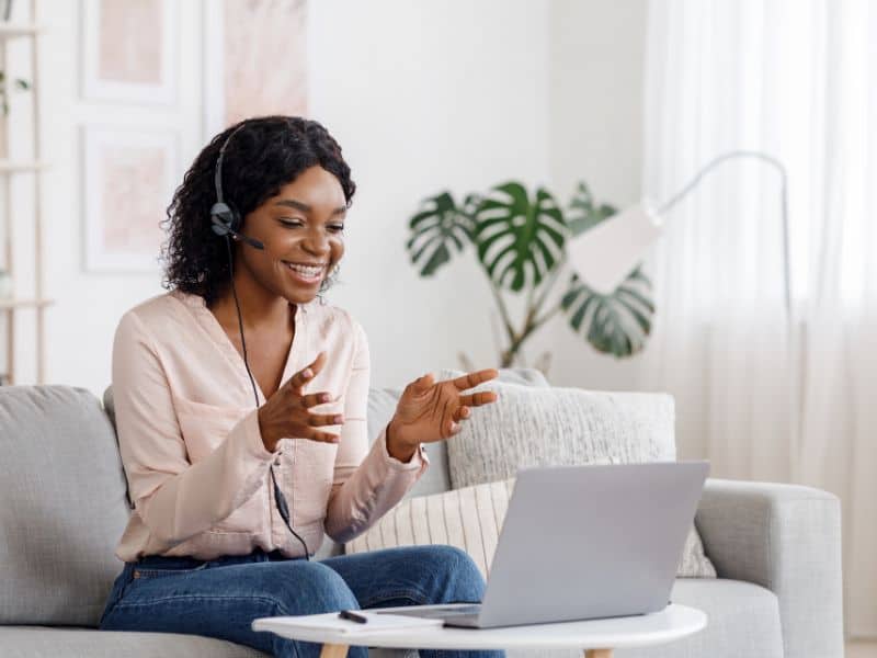 Woman sitting on a sofa with a headset on and talking at her laptop