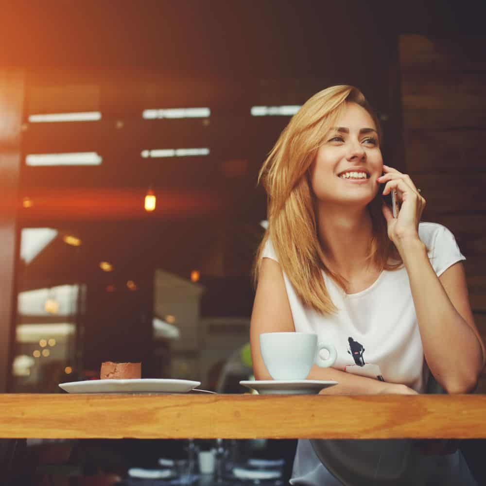 Young woman in a cafe speaking on her phone and smiling