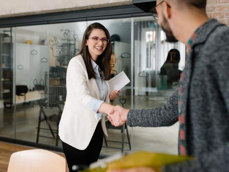 Photo of young woman shaking someone's hand in an office