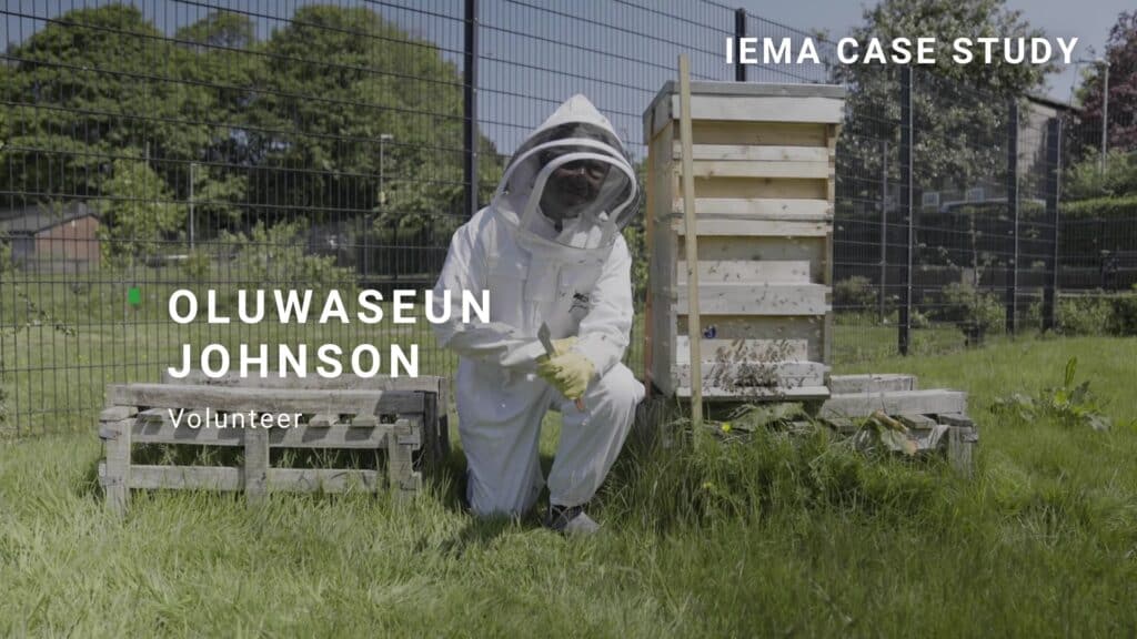Photo of Oluwaseun Johnson in beekeeping outfit, outside next to the bee hives