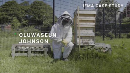 Photo of Oluwaseun Johnson in beekeeping outfit, outside next to the bee hives