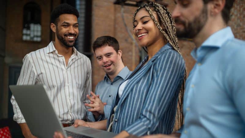Four people looking at a laptop screen and smiling