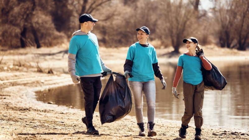 Three volunteers walking along some water with bin bags of rubbish