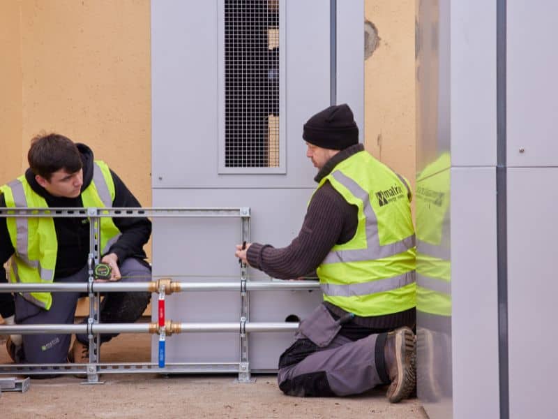 Two men in high-visibility jackets working on heat pumps