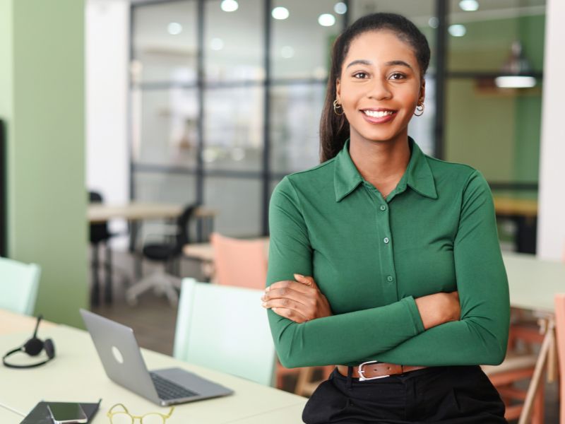 Woman dressed in a green shirt stands smiling in an office