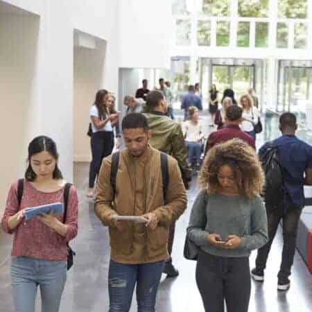Photo of students in a hallway looking at phones or tablets