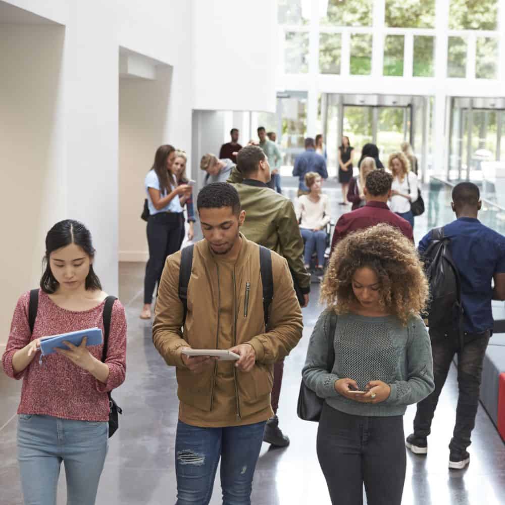 Photo of students in a hallway looking at phones or tablets