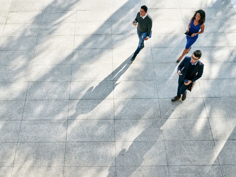 Aerial shot of three people walking outside on a grey pavement
