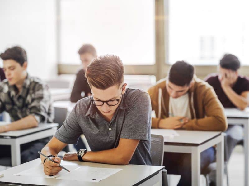 Photo of a group of young students completing exams at tables