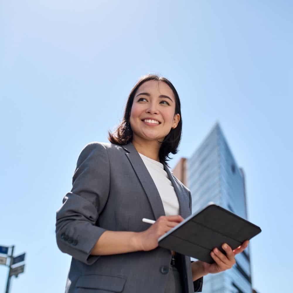 Photo of a young woman with an ipad with a skyscraper behind her