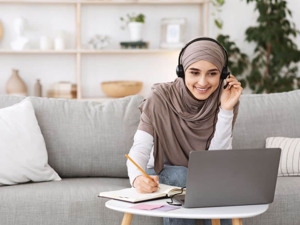 Photo of a young woman wearing a headscarf and on a virtual call at her laptop