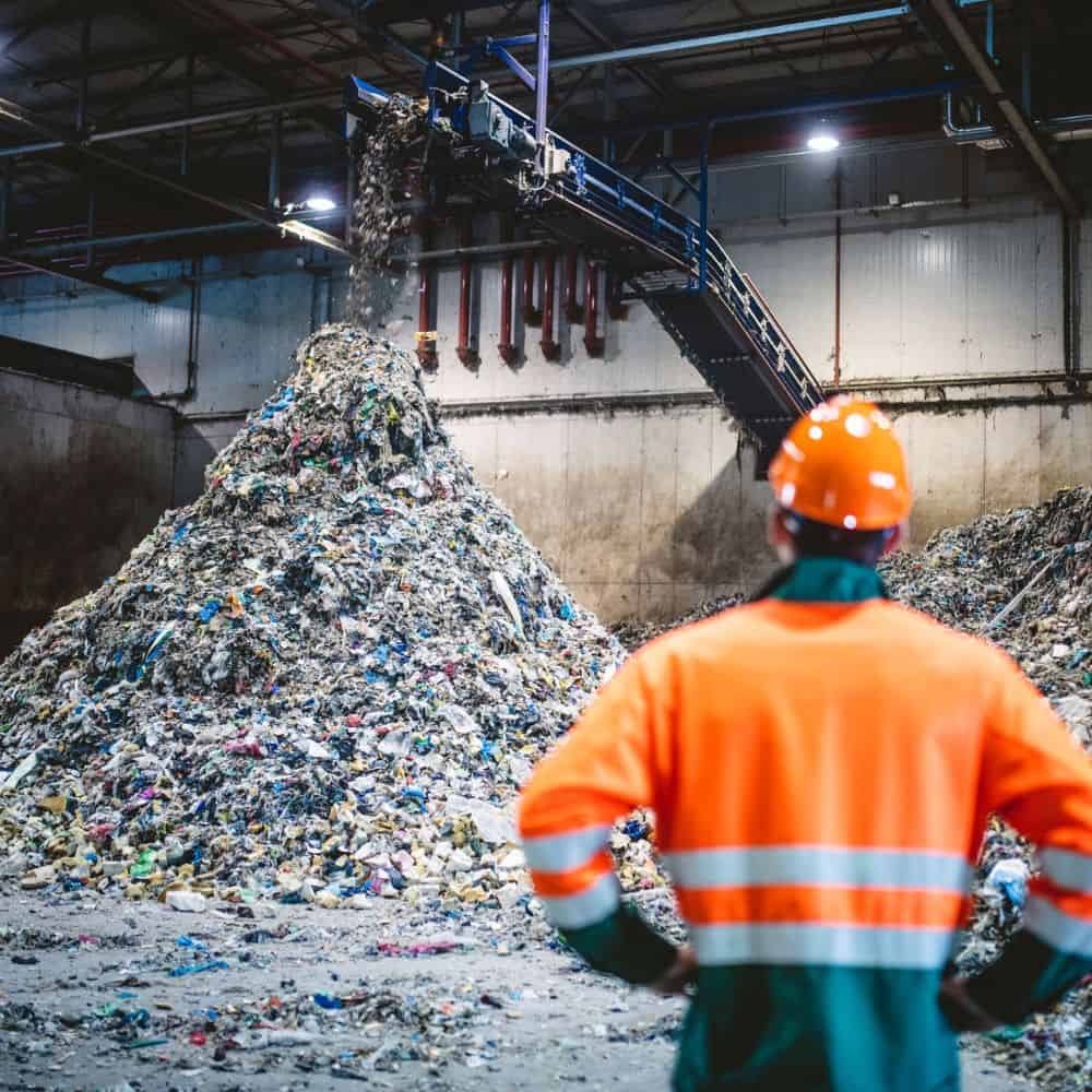 Man in a high-visibility jacket and hard had standing looking at a pile of waste in a sorting plant