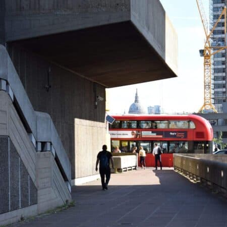 Photo through buildings in London, with St Pauls cathedral in the background, and a red London bus