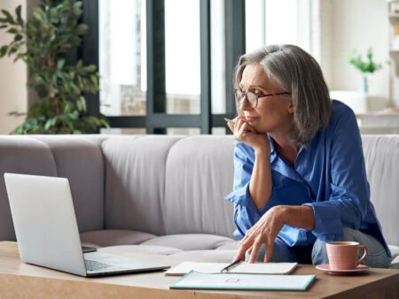 A woman is sat looking at her laptop screen whilst sat on a sofa