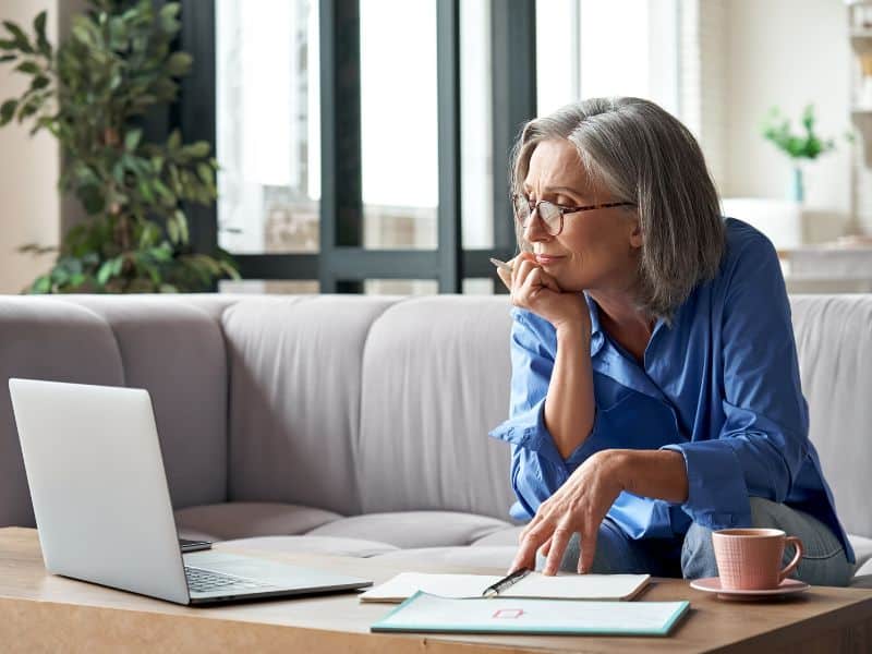 A woman is sat looking at her laptop screen whilst sat on a sofa