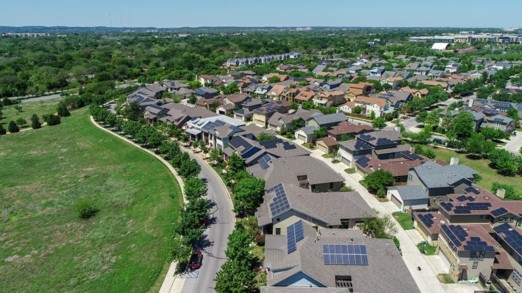 Aerial view of a residential street with green fields alongside