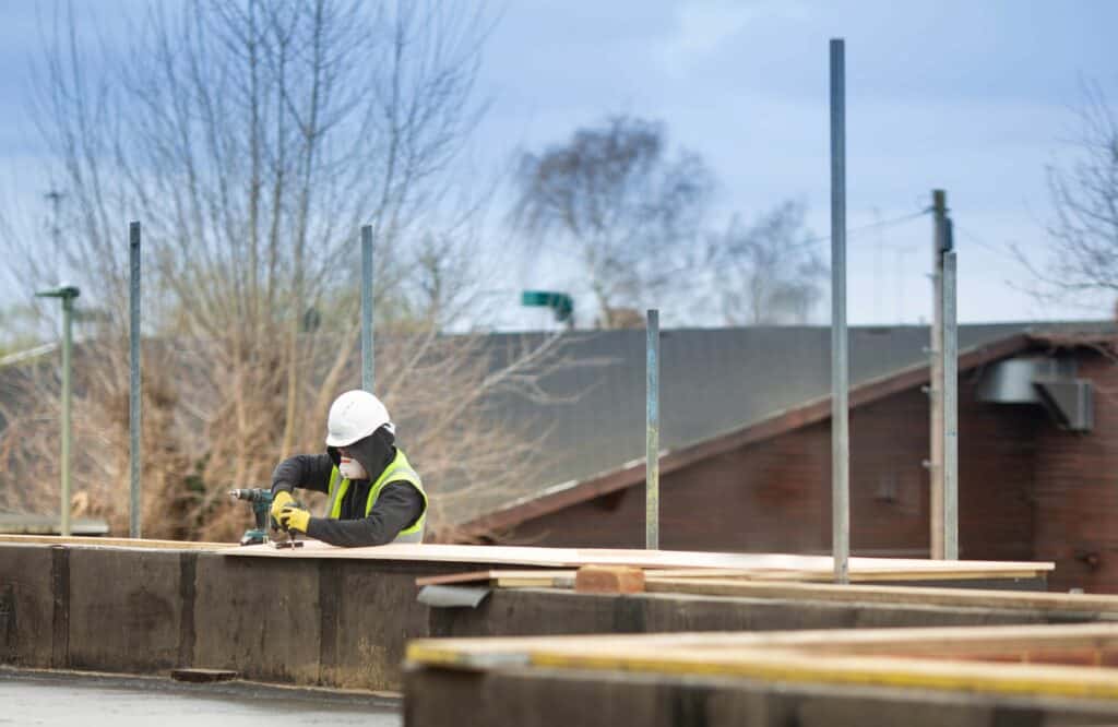 A worker in a high-vis jacket and a hard hat working on top of a building