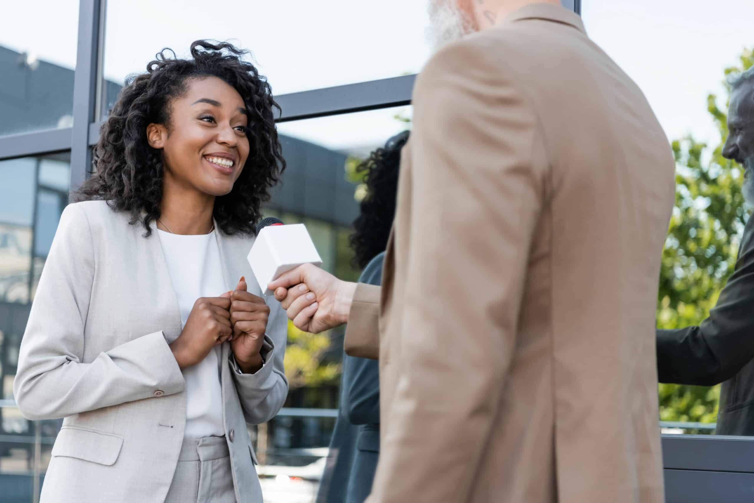 Photo of a woman being interviewed by somebody else, with a microphone being held in front of her