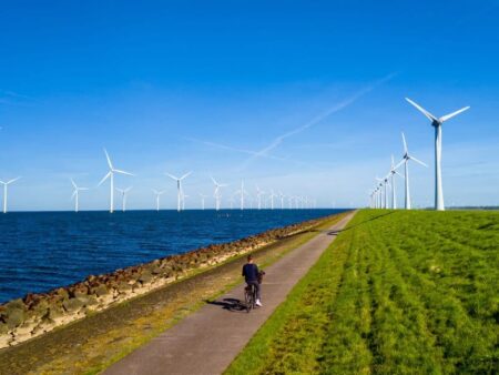 Person cycling along a coastline with wind turbines in the background
