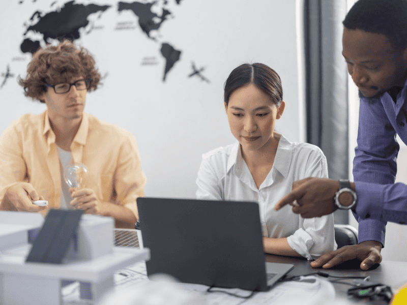 Three people looking at a laptop. One person is holding a light bulb