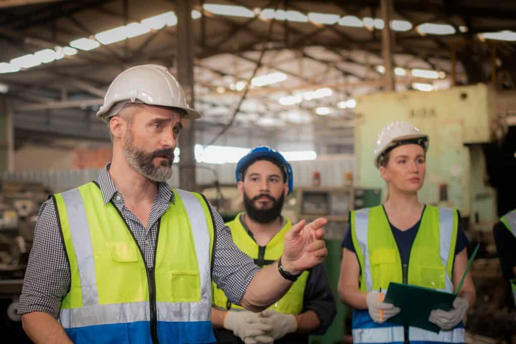 Three people in high-visibility jackets and hard hats inside a building