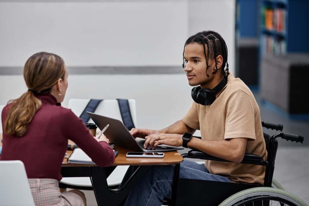 Two younger people sat working collaboratively at a desk with laptops