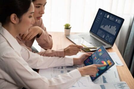 Two people in an office looking at data and graphs on two devices