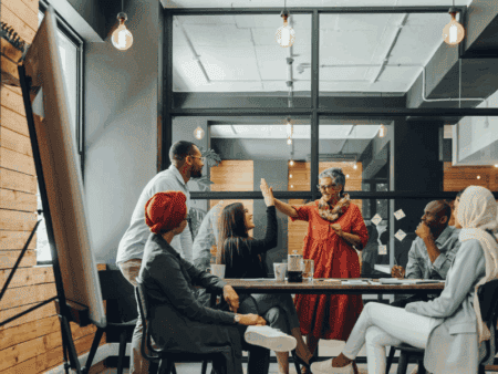 Group of people in a meeting room, two of them are in the middle of a high-five gesture