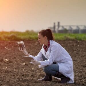 woman taking soil sample in a field. she is wearing a white coat