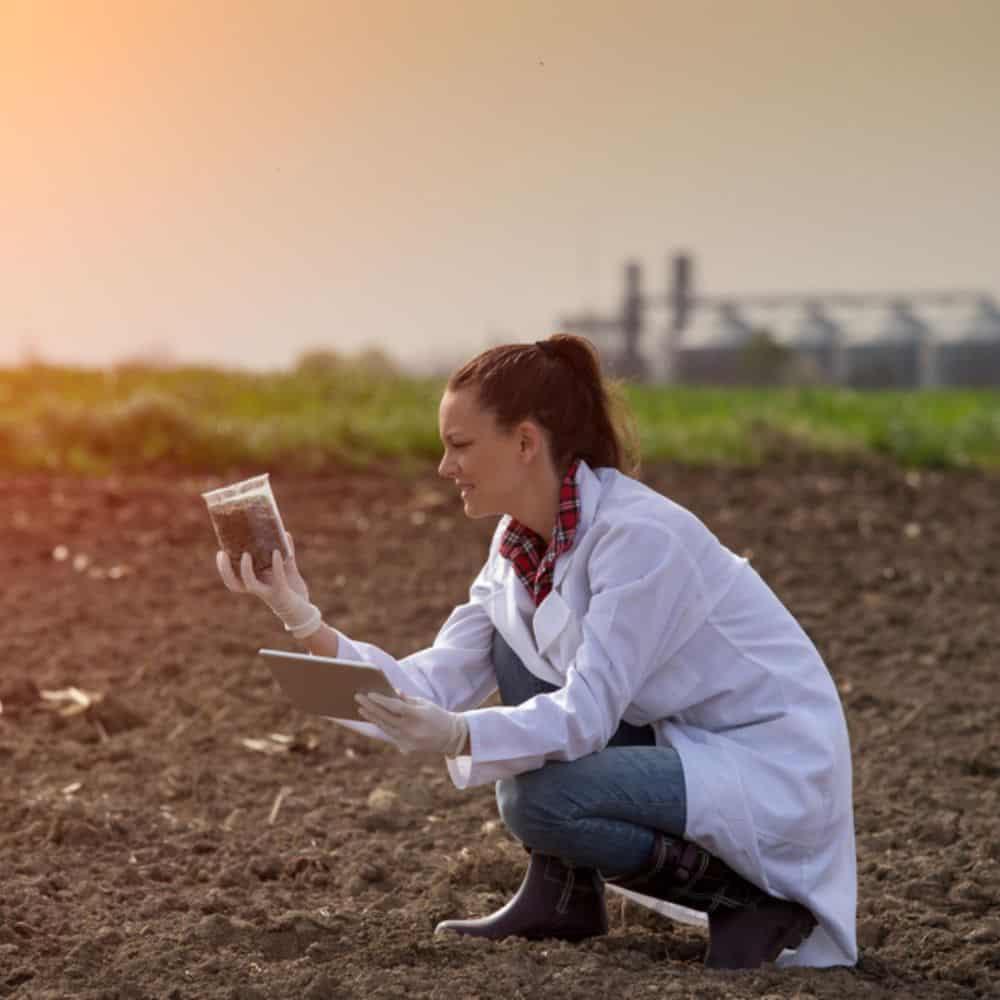 woman taking soil sample in a field. she is wearing a white coat