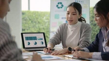 woman speaking to colleagues and showing them graphs on a computer screen