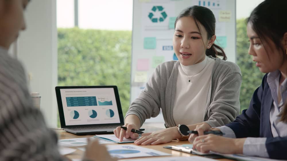 woman speaking to colleagues and showing them graphs on a computer screen
