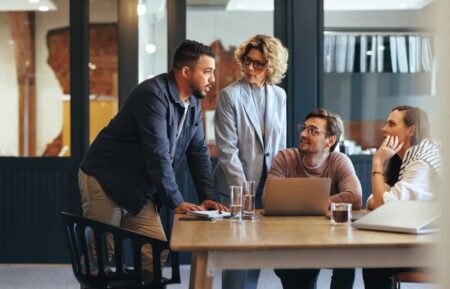 People talking in an office space around a laptop